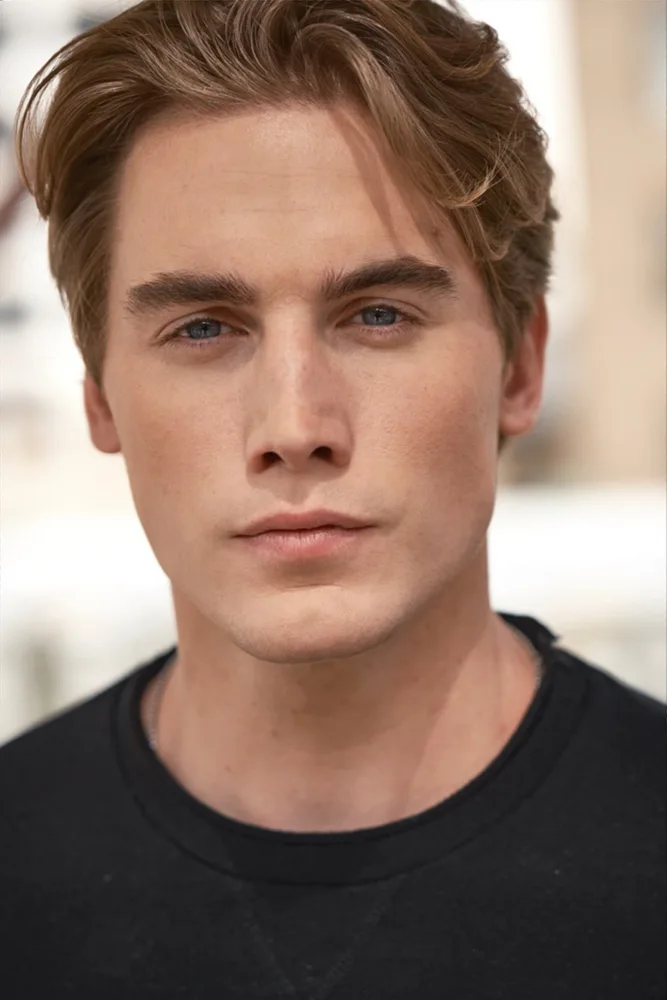 Nick with longer hair, in a charcoal shirt outdoors
